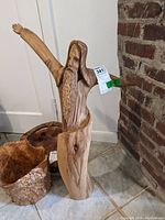 Full view of the tall wooden Jesus figure standing on the ground with one arm extended up, next to two wooden bowls.