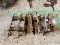 Three pairs of antique ice skates arranged on floor showing metal blades with various leather straps and mounts.
