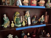 Wide shelf view of Asian ceramics like figurines, bud vases, and a tea pot with various colors and designs.
