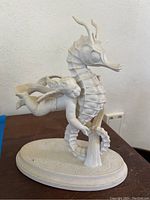 Front angle showing cherub hugging seahorse on oval base with hexagonal pattern, white porcelain detailing.