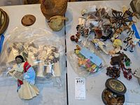 Overall lot showing corn husk dolls wrapped in plastic bag on the left and assorted folk art animal figures on right, plus woven basket and wooden painted box