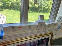 Seven white boxes of Department 56 Heritage Village Collection lined up on a window sill, showing boxed figurine collections and accessories with some readable labels like 'Sleepy Hollow'.