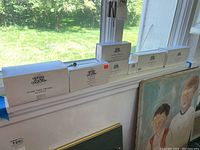 Seven white rectangular boxes labeled The Heritage Village Collection by Department 56 placed on a windowsill.