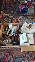 Box containing assorted vintage doll house furniture pieces and small accessories on a patterned rug.