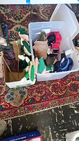 Overall view of handmade puppet and seven winter-themed dolls in two storage bins on a patterned rug showing variety of dolls and puppets.