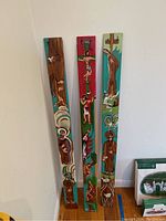 Photo showing three tall vertical wood slats painted with religious scenes leaning against a white wall.