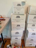 Stack of several boxed collectible porcelain houses from the Heritage Village Collection New England Village Series showing box labels and packaging condition.