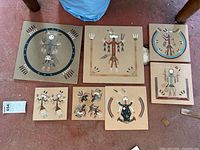 Overview of the seven Navajo sand art pieces arranged on floor, showing variety in size and designs.