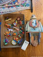 Photo showing multiple colorful wooden animal ornaments in a box and the large Bird Man figure beside it.