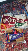 Top view of multiple vintage pennants including Penns Grove, Ocean City NJ, Sweet Briar, and Asheville School inside a box and spread over carpet.