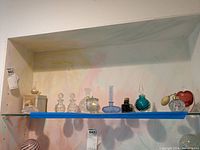 Shelf displaying all nine perfume bottles including various colors and shapes with two atomizer bottles