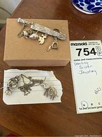 Photo showing all three jewelry items on a brown box and paper: sword pin with hanging charms, round pendant with broken chain, and elephant pin on white card.