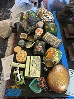 Photo showing assortment of ceramic, metal, wood, and stone trinket boxes in various shapes and decorations on black surface