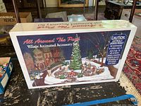 Image of the sealed box showing a winter village animated scene around a large Christmas tree with skating figures and park buildings.