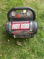 Front view showing the 5 gallon tank with Powerbuilt Hot Rod label and control panel with pressure gauges and red knob.