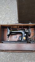Antique Singer sewing machine visible inside wooden case, machine black with gold decals.