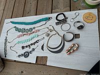 Assorted costume jewelry laid out on white board including beaded necklaces, bracelets, rings, a metal cuff, and keychain.