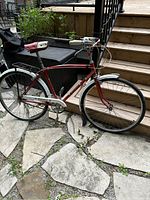 Full side view showing the vintage red bike with white and red saddle, handlebar grips, and metal fenders on stone patio near steps.