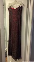 Full length photo of the strapless black sequin dress with red silk underlay hanging on hanger