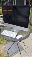 Apple iMac computer set on a small metal patio table outdoors, includes keyboard and mouse.