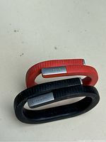 Two Jawbone UP fitness trackers, one orange small and one black medium, placed overlapping on a light surface.