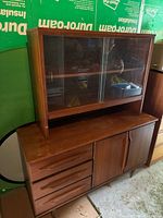 Front view of two-piece wooden hutch buffet showing drawers, cabinet doors, and glass-door top