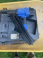Blue Campbell Hausfeld 2-in-1 brad nailer lying in an open black molded carrying case, placed in a yellow wheelbarrow.
