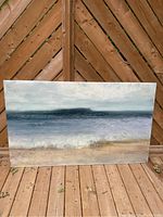 Front view of large rectangular painted sandy beach poster on acrylic mounted against wooden backdrop, showing muted shades of blue, gray, beige and white in ocean and sky scene.