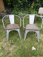 Front view of two metal and wood arm chairs placed on grass showing curved armrests and wooden seats.