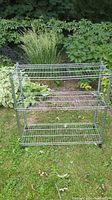 Front view of chrome steel wire shelving unit with three wire grid shelves, placed outdoors on grass with greenery in the background.