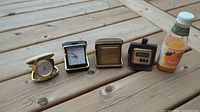 Four vintage travel alarm clocks folded open and closed on wooden surface, showing size comparison next to a small juice bottle