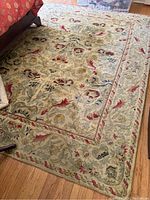 Full view of wool area rug laid on hardwood floor, showing detailed floral border and colors.