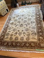 Full view of the beige and brown floral patterned area rug with fringe on a hardwood floor.