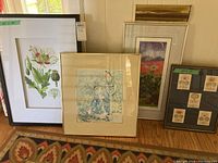 Four framed artwork pieces displayed leaning on a couch with a patterned carpet beneath, showing varying sizes and frame styles.