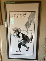 Full view of the framed Asian themed artwork showing an elderly fisherman carrying a fishing rod with a large fish, with calligraphy in the upper left corner.