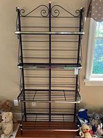 Front view of black metal bakers rack with gold trim and four shelves, showing overall design and condition.
