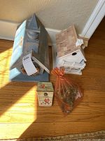 Both birdhouses, the small decorated wooden box with heart design, and the orange mesh bag with decorative branches and string lights all placed on wooden floor.