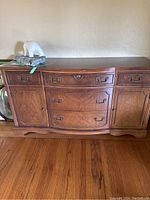 Front view of the vintage wooden buffet cabinet showing three drawers in the center, two drawers on the sides, and two cabinet doors on each side with metal handles.
