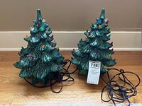 Two ceramic Christmas trees side by side on hardwood floor showing cords and bases