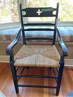 Front view of glossy black wood framed chair with woven seat under natural light