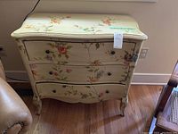 Front view of cream colored painted three-drawer chest with floral design