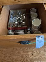 Overall view inside drawer showing ceramic mugs, flatware, napkin rings and glass shakers