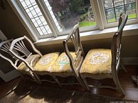 Four dining chairs lined up by window showing carved wooden frames and upholstered seats.