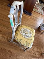 Close-up photo of one dining chair showing floral upholstered seat and distressed white wooden frame