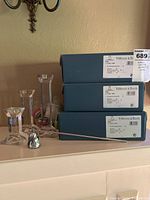 Three pairs of Villeroy & Boch Pisa glass candlestick holders with boxes stacked behind and a metal candle snuffer with handle in front.