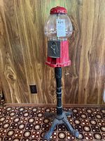 Full view of the vintage red gumball machine on its black ornate cast iron stand showing overall shape and condition.