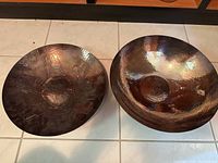 Two bowls side by side on tiled floor: left etched bowl with ornamental motif, right plain hammered bowl