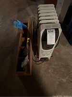 Overview photo showing electric heater beside wooden tool holder on basement floor.