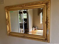 Full view of the large rectangular mirror hung on a beige wall reflecting part of the room and window.