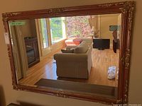 Full view of a large rectangular beveled mirror reflecting a living room scene with couch, TV, and windows.